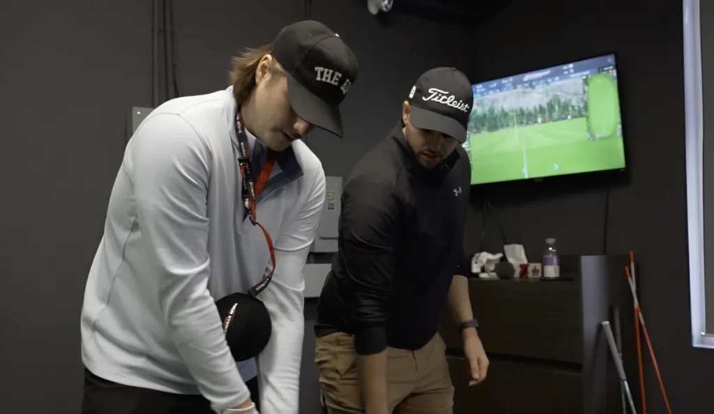 A golf instructor and student reviewing swing data on a screen during an indoor training session.