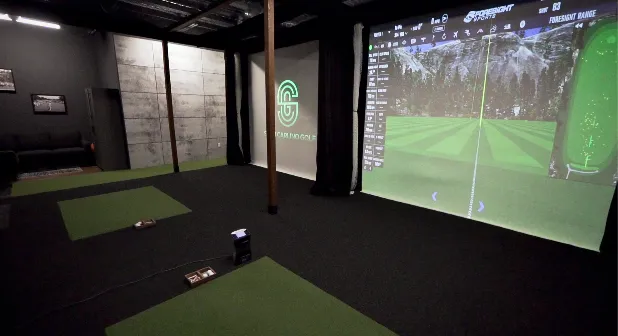 An indoor golf simulation facility featuring hitting mats and a large screen displaying a virtual fairway.