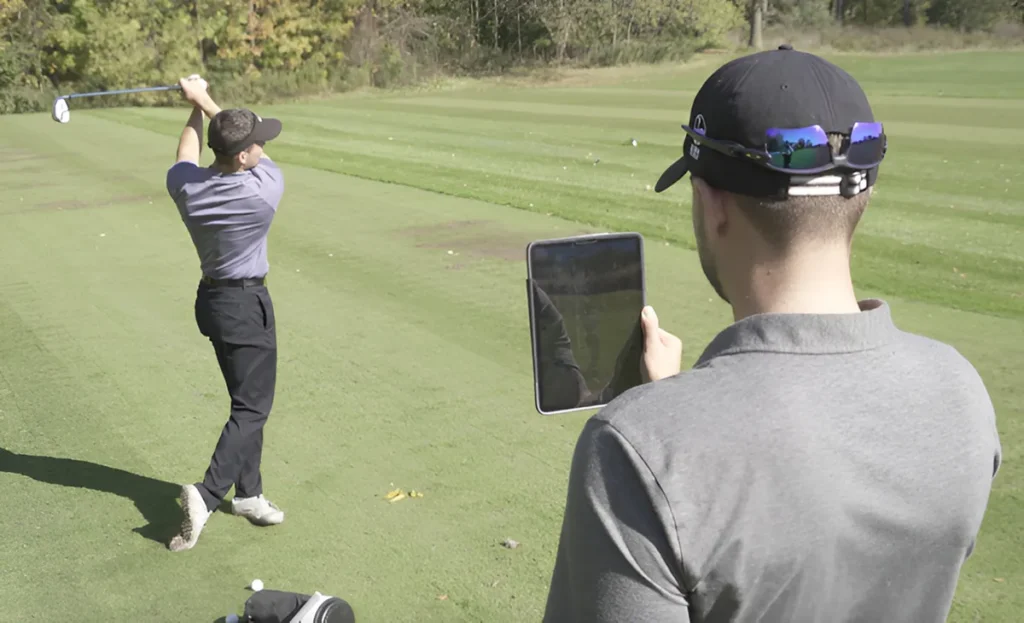 A golf instructor using a tablet to record and analyze a student's swing during an outdoor lesson.