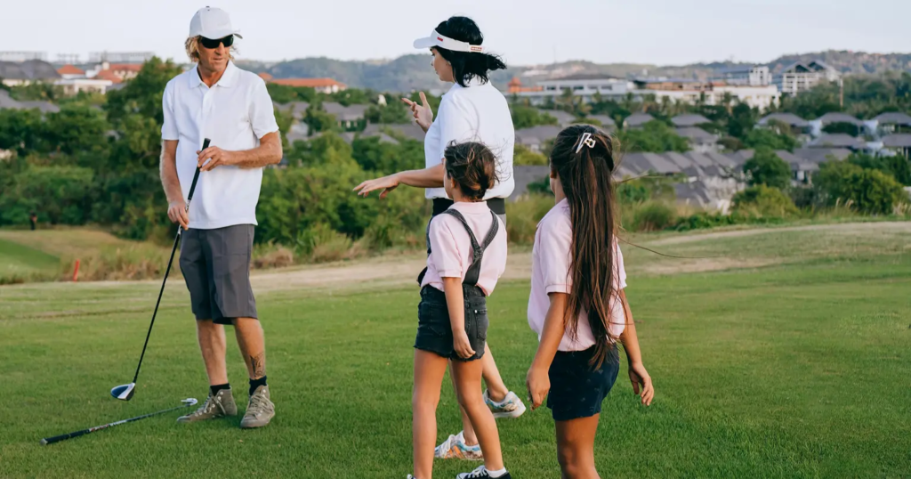 A golf instructor talking to a woman and two young girls on a green.