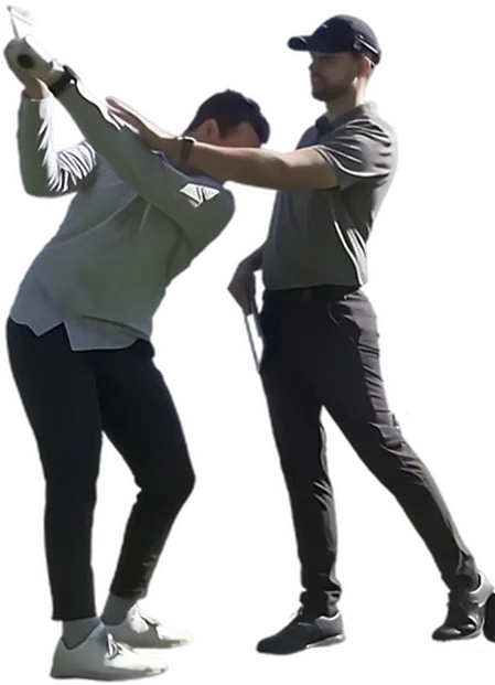 A golf coach in a grey polo and black cap adjusting a student's posture during a backswing practice session.